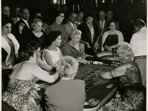 Female gamblers in elegant dresses and fur stoles at the roulette table in the Sands Hotel. 