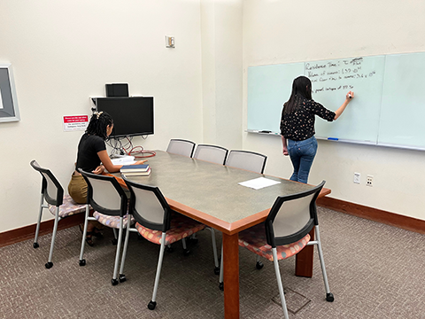 Students sitting at table and writing on glassboard in study room.