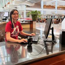 A student sits at a computer at the Circulation Desk in Lied Library.