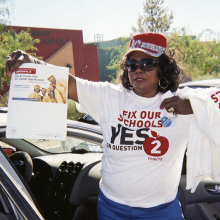 Marzette Lewis holding a sign and wearing a shirt that reads, "Fix our schools, say yes to question 2"