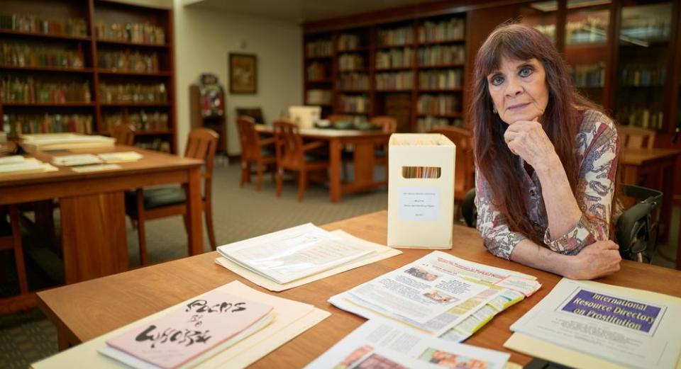 A woman sits at a table in a library with documents spread out in front of her.