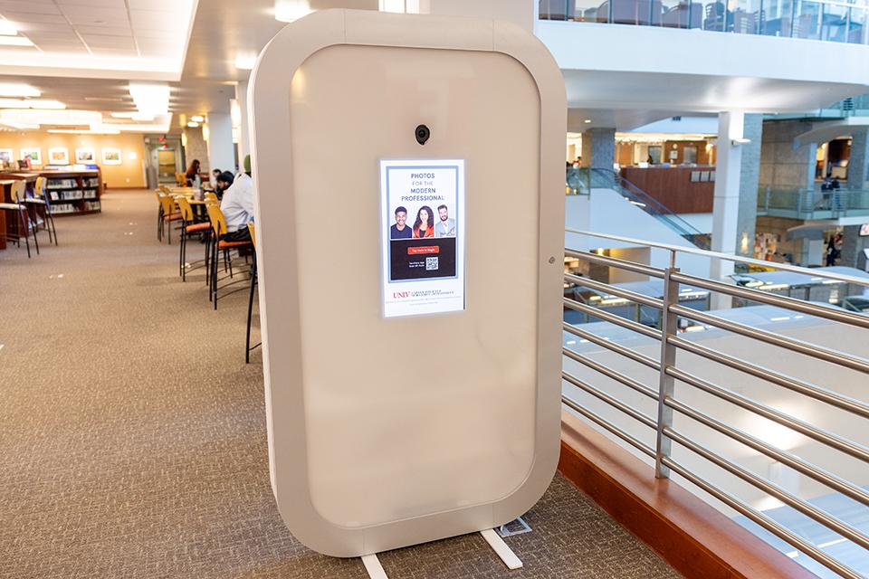 Photo booth kiosk in a public library with tables and people studying.