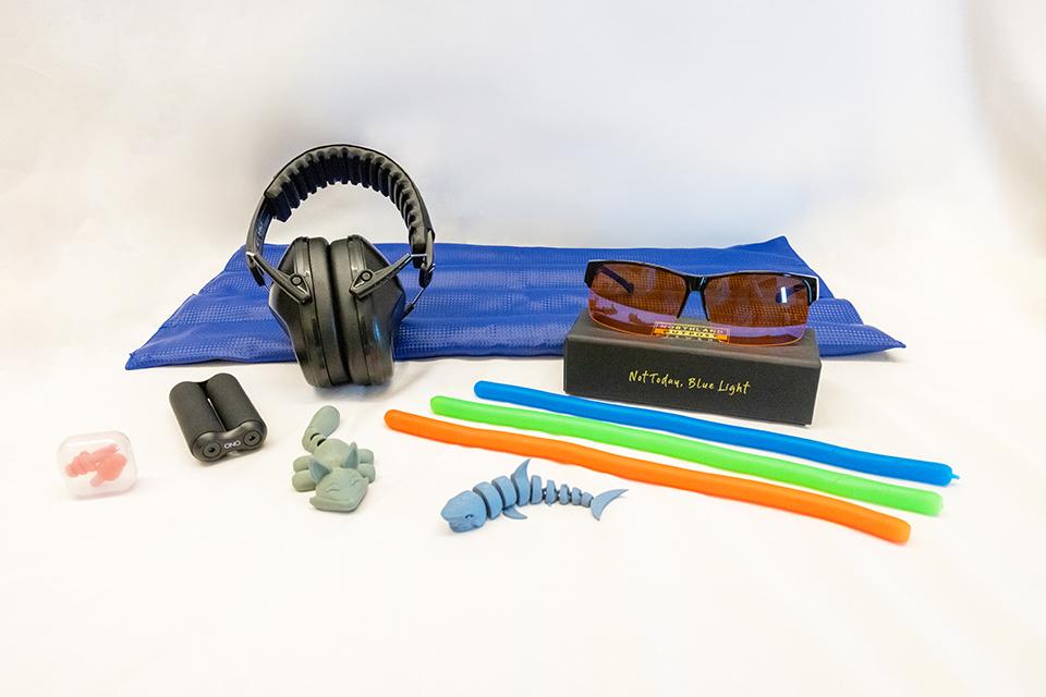 Various relaxation and sensory items available at Lied Library, including headphones, blue light glasses, flexible sticks, and earplugs on a blue mat.