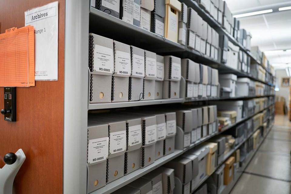 Collapsible archive shelves filled with white labeled boxes. Close-up of a wooden shelf panel with a sign reading 'Archives Range 1'.