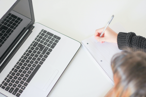 Student at desk with notepad and laptop