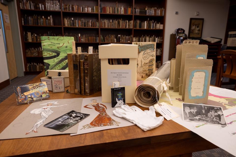 A table in a library covered with archival materials, books, and vintage illustrations.