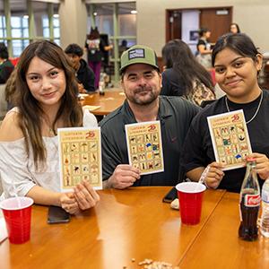 Three people hold up their Loteria cards.