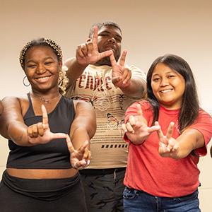 Three people shape their fingers to make an L and a V.