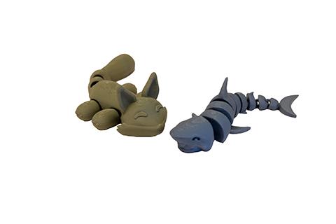 Two 3D-printed articulated fidget toys: a green fox with movable arms and tail, and a blue segmented shark.