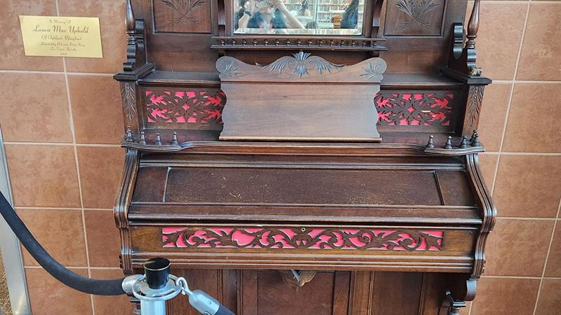 Vintage wooden organ with ornate carvings and red detailing against a tiled wall.