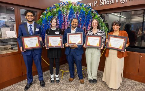 Five people holding certificates stand in front of a colorful flower backdrop.