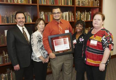 Group photo with winner holding framed award certificate.