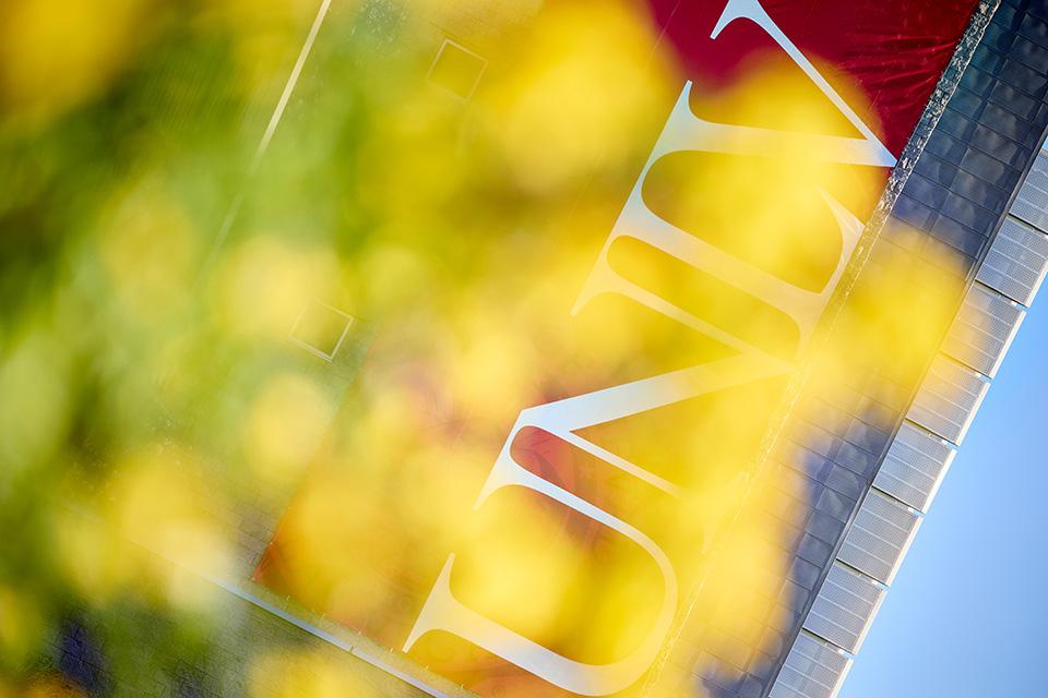 A UNLV banner on the side of Lied Library behind leaves on a tree.