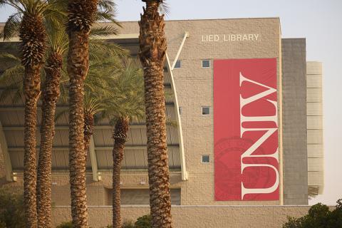Exterior of Lied Library with a vertical red banner and palm trees in front.