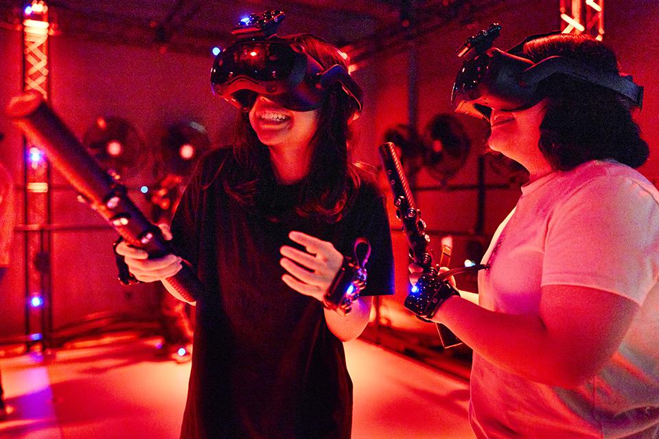 Two people wearing virtual reality headsets and holding controllers in a red-lit room.
