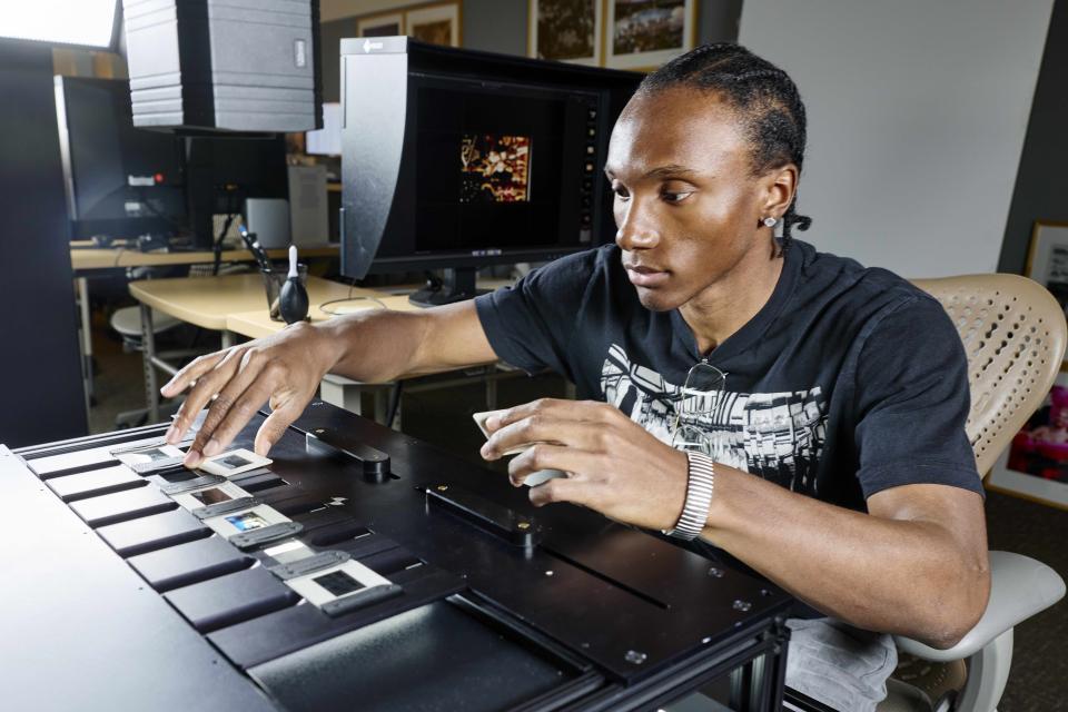 Student placing photographic slides into a digitization scanner in a lab setting.