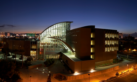 Modern building with a curved glass facade and brick structure lit up at dusk.