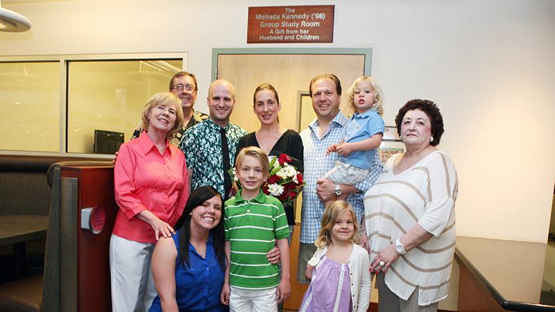 A group of 10 people of varying ages stand in front of a group study room.