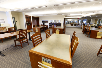 The outer reading room of Special Collections and Archives with wooden tables and chairs, carpeted floor, and a background of bookshelves and computers.