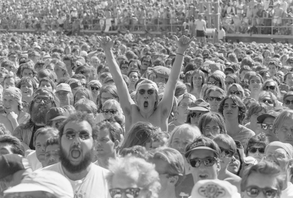 One person stands in a large crowd with their hands raised in excitement. The crowd was gathered to see the Grateful Dead in concert at the Silver Bowl on April 27, 1991.