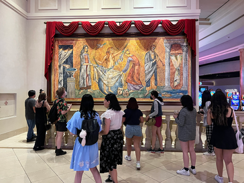 Photo of students looking at a faux roman mosaic in the Caesars Palace casino - there are slot machines in the background. It shows the use of ancient Roman imagery as decor in the Casears Palace casino. 
