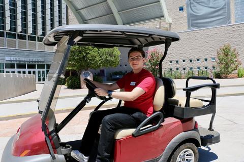 A student driving a golf cart outside Lied Library.