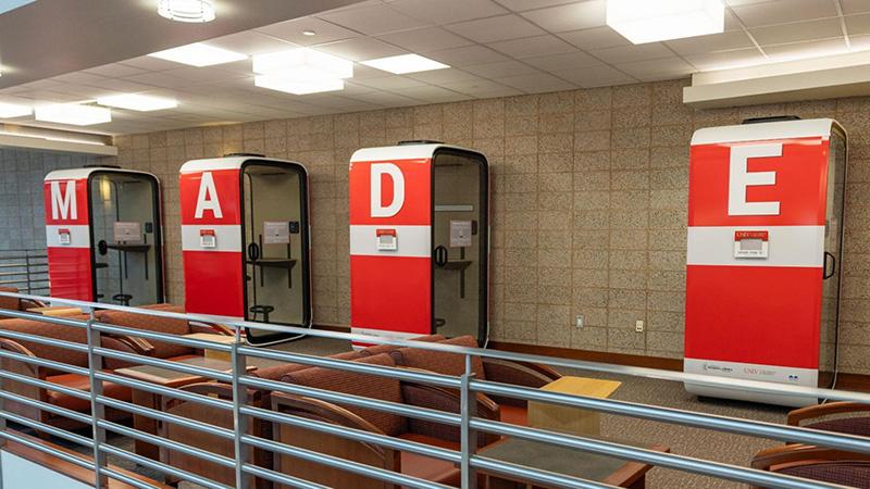 Four red and white study pods with letters M, A, D, E on a tiled indoor wall.
