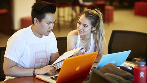 Two students talking while using laptops.