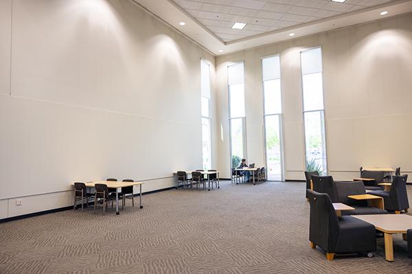 A spacious event on the library's first floor with tables, chairs, and tall windows.