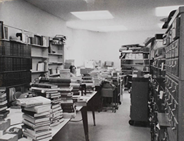 Black and white interior photo of Grant Hall Library showing books stacked on tables and card catalog drawers.