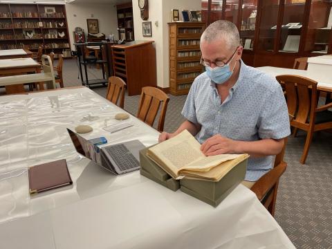 Dr. John Elgin sitting at a table with a laptop examining a historical book