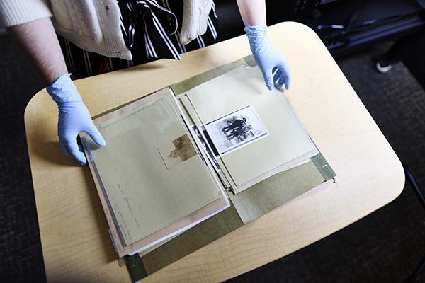 A person wearing gloves showing a folder with Special Collections archival documents and photographs.