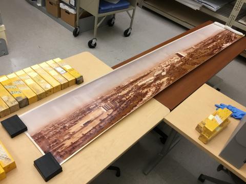 A long panoramic photograph of the Las Vegas valley unrolled across two tabletops. The image is printed in color and held down using weights.)
