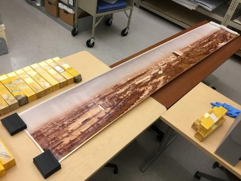 A long panoramic photograph of the Las Vegas valley unrolled across two tabletops. The image is printed in color and held down using weights.)