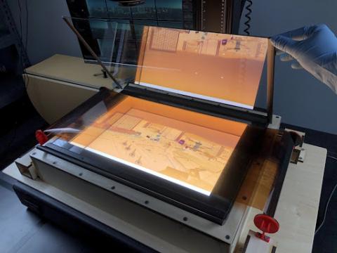 A piece of glass being placed on top of a negative to help keep the negative flat during digitization. The negative depicts the Las Vegas Strip and is stretched across the glass carrier held by a wooden base