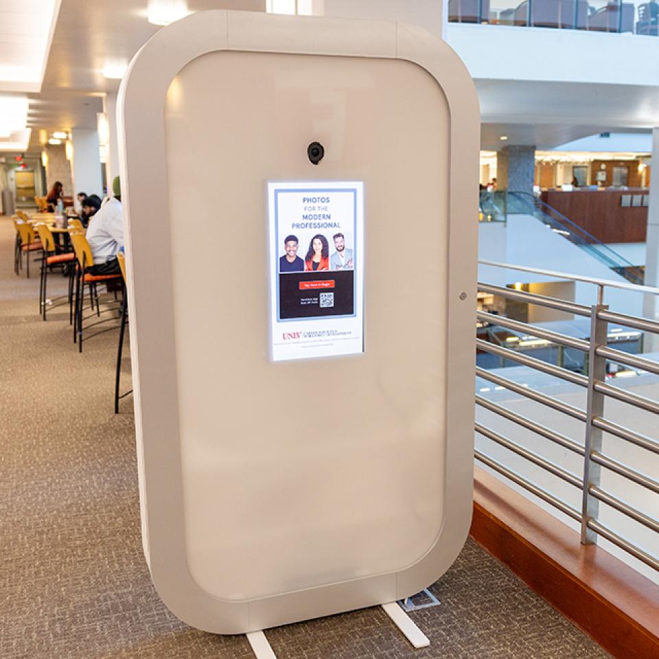 Photo booth kiosk in a public library with tables and people studying.