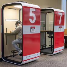 Two red and white study pods numbered 5 and 7 with a person working inside pod 5.