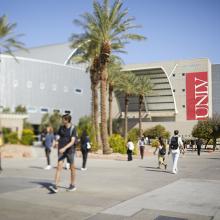 Students walk on a university campus with a building displaying a "UNLV" banner.