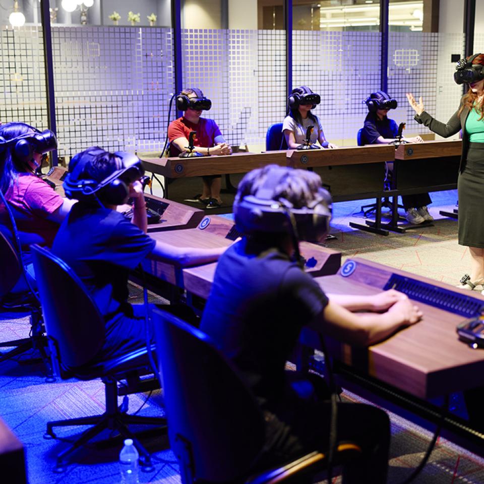A classroom with students wearing VR headsets seated at desks, facing an instructor.