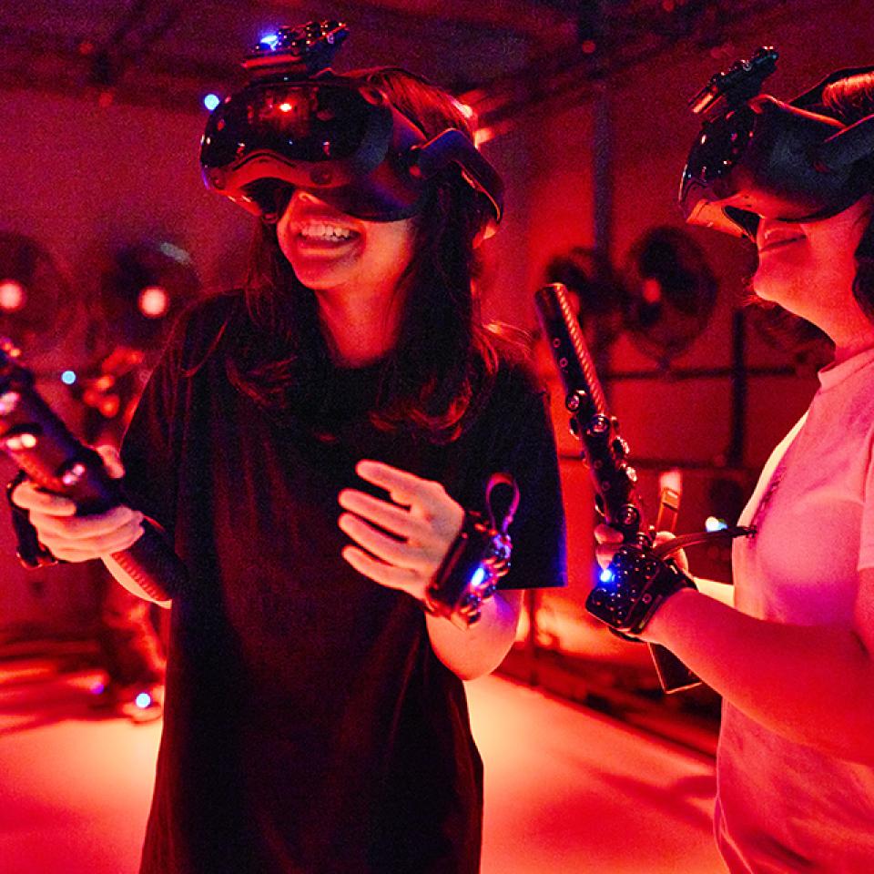Two people wearing virtual reality headsets and holding controllers in a red-lit room.