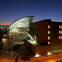 Modern building with a curved glass facade and brick structure lit up at dusk.