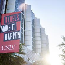 Red banner with text "REBELS MAKE IT HAPPEN UNLV" in front of Lied Library