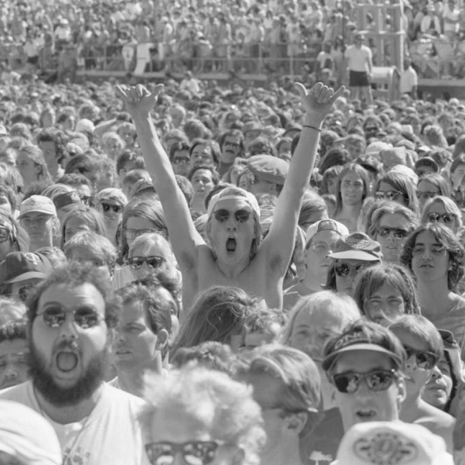 One person stands in a large crowd with their hands raised in excitement. The crowd was gathered to see the Grateful Dead in concert at the Silver Bowl on April 27, 1991.