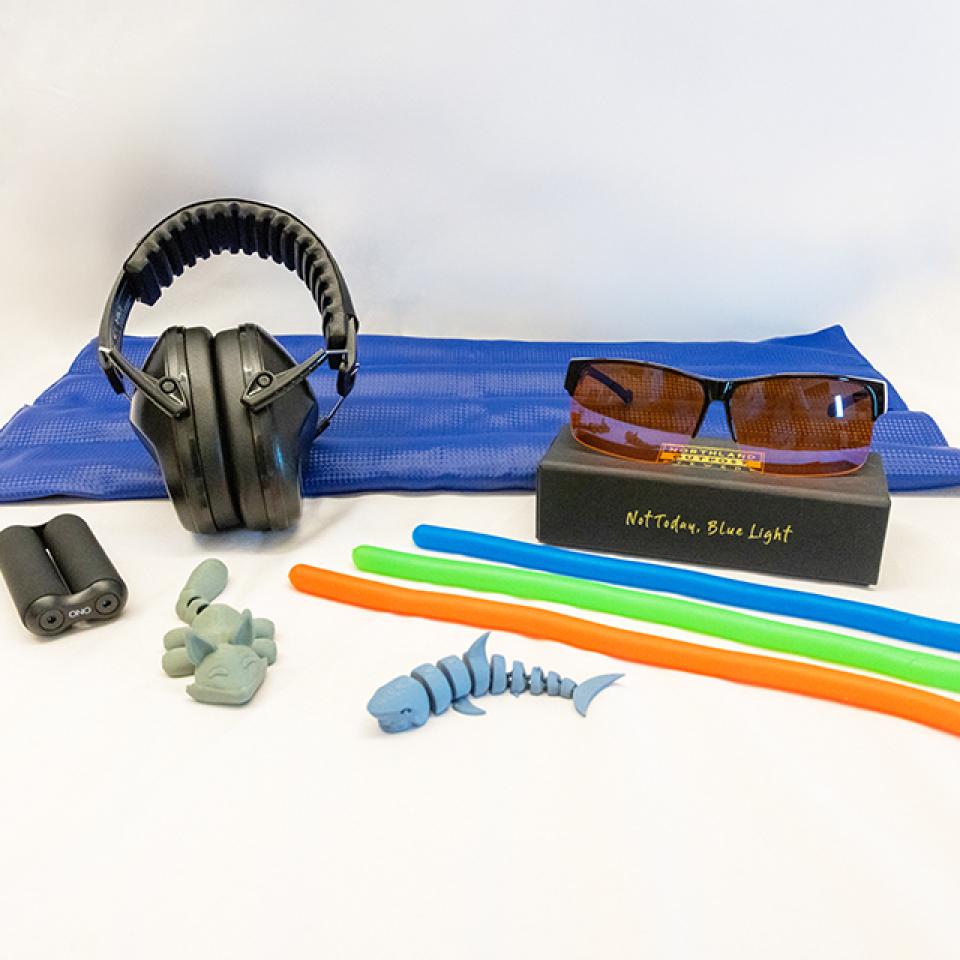 Various relaxation and sensory items available at Lied Library, including headphones, blue light glasses, flexible sticks, and earplugs on a blue mat.