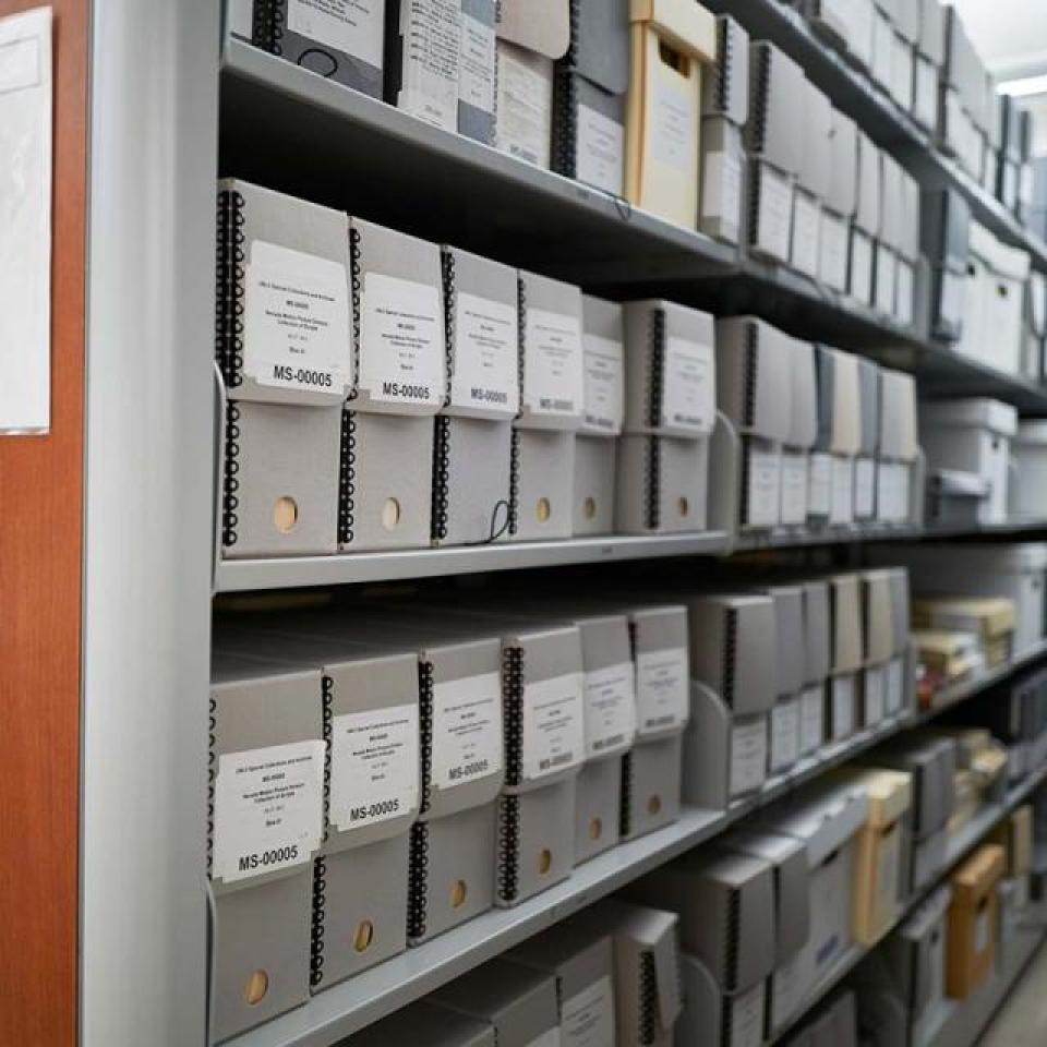 Collapsible archive shelves filled with white labeled boxes. Close-up of a wooden shelf panel with a sign reading 'Archives Range 1'.