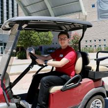 A student driving a golf cart outside Lied Library.