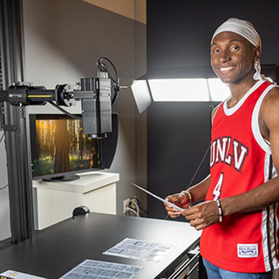 Person in a red "UNLV" jersey standing next to scanning equipment in a studio setting.