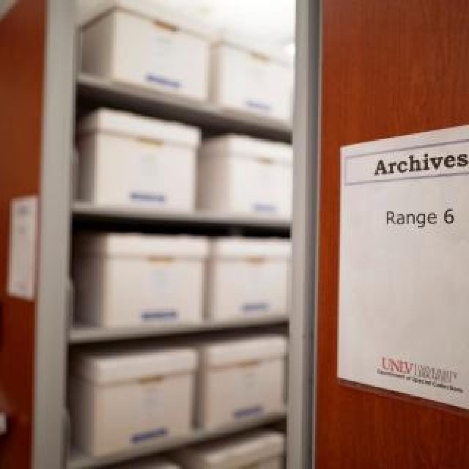 Collapsible archive shelves filled with white labeled boxes. Close-up of a wooden shelf panel with a sign reading 'Archives Range 6'.