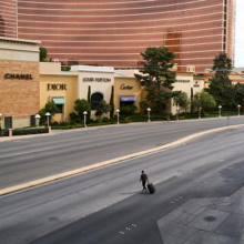 Man pulling wheeled luggage walking across empty Las Vegas Blvd