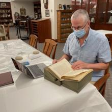 Dr. John Elgin sitting at a table with a laptop examining a historical book